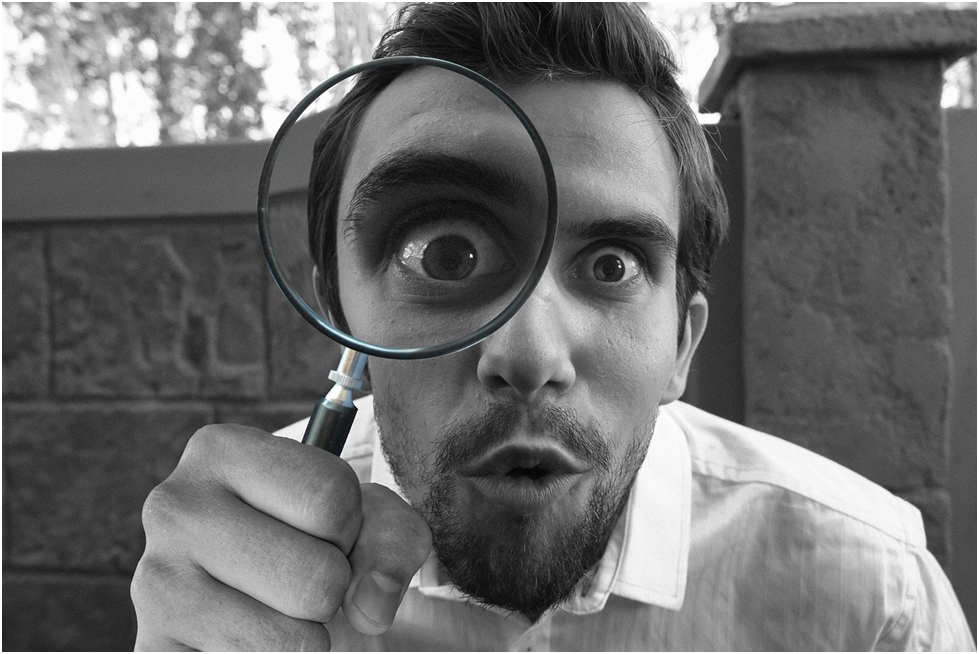 MAN LOOKING THROUGH A MAGNIFYING GLASS PAYING ATTENTION TO DETAIL